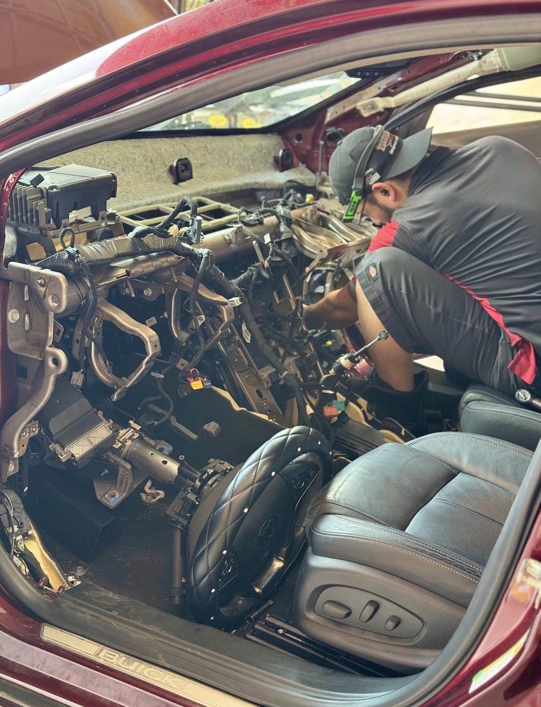 Burgundy Buick with the entire dashboard removed and the wiring harness exposed while a technician works inside the cabin