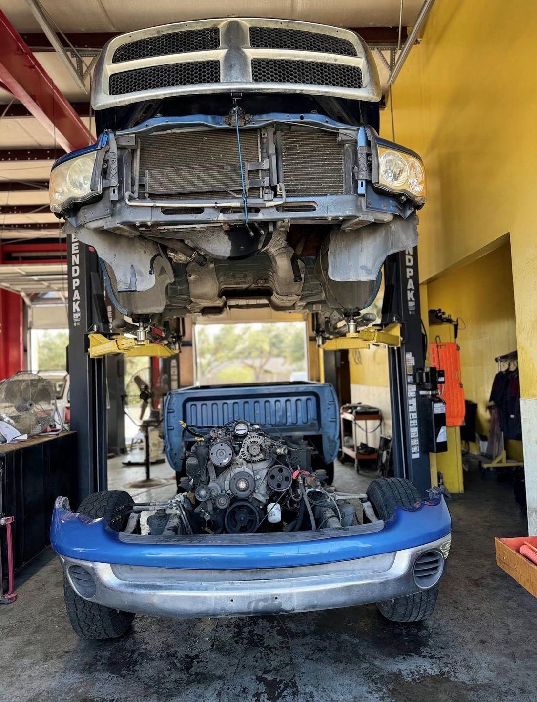 Blue Dodge Ram raised on a BendPak lift with the front end removed and the engine resting on the shop floor